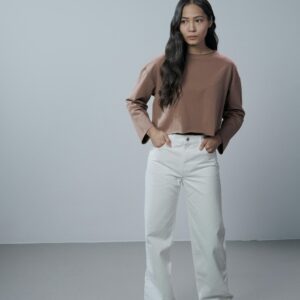 Portrait of a fashionable woman in casual clothing standing in a minimalist studio.
