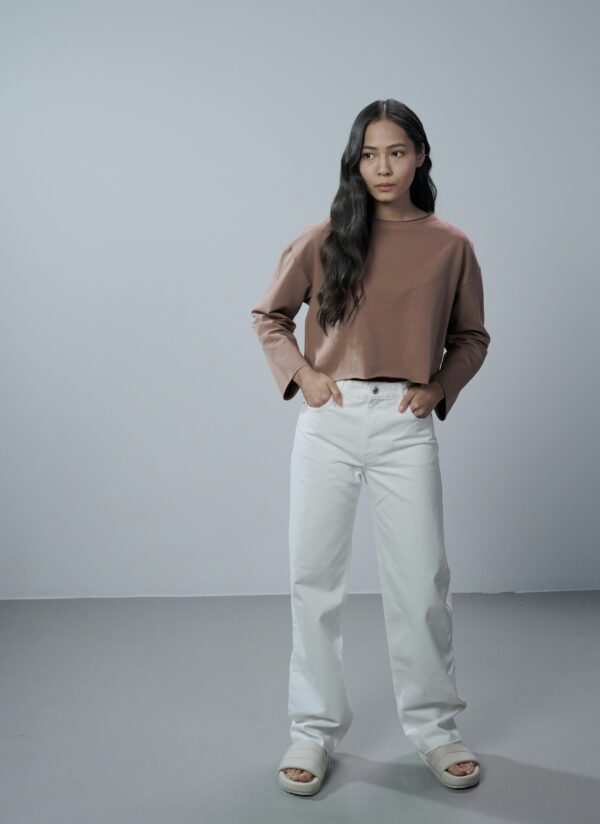 Portrait of a fashionable woman in casual clothing standing in a minimalist studio.